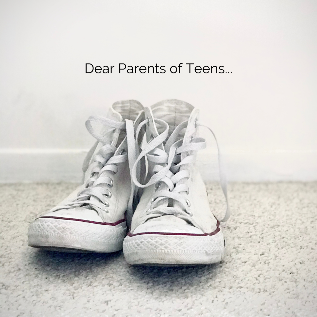 A pair of high top tennis shoes on the ground with the words Dear Parents of Teens written on the wall.